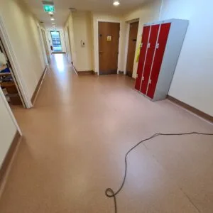 Beige vinyl safety flooring in a corridor near storage lockers, freshly cleaned