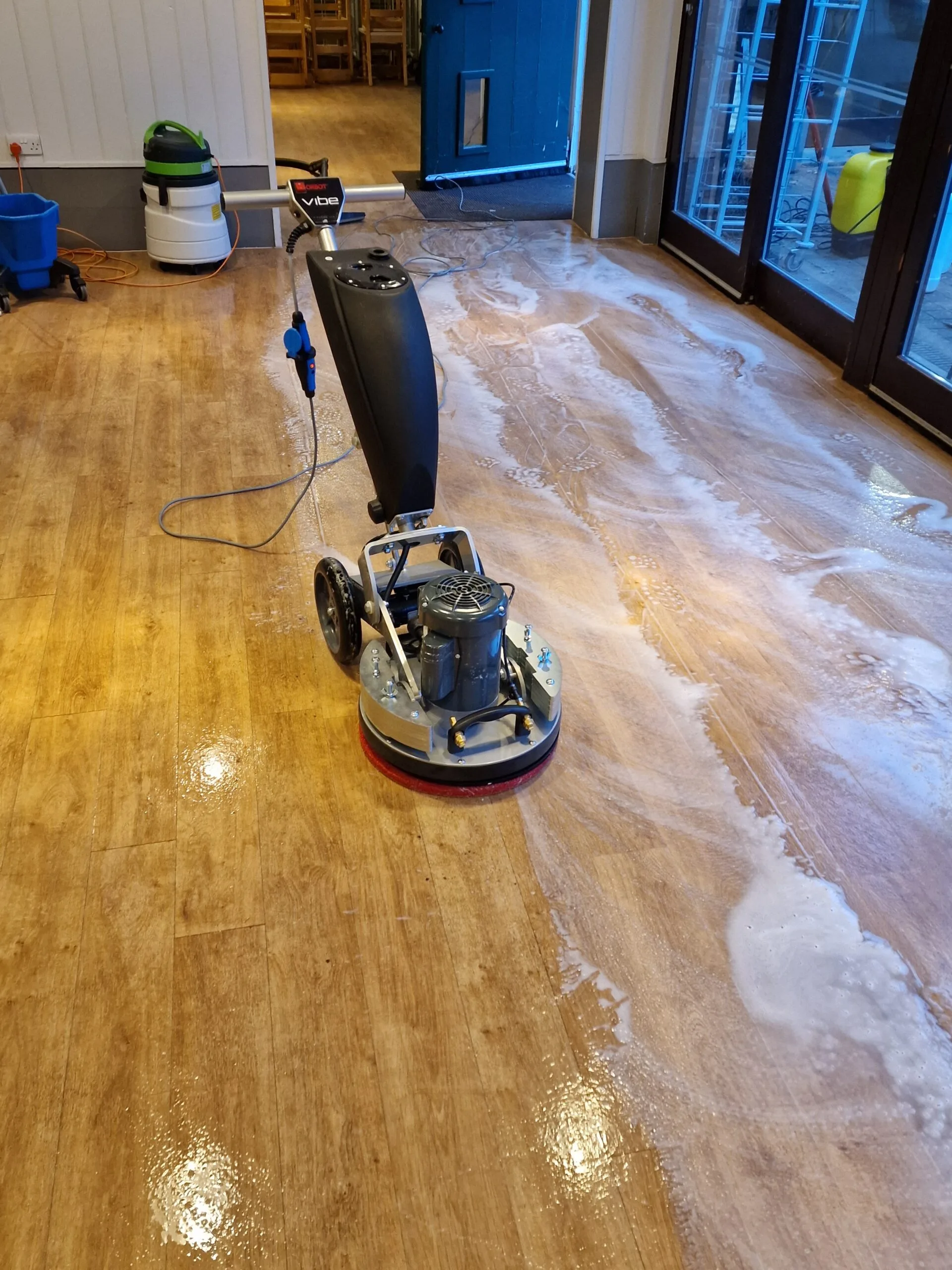 Rotary buffing machine polishing a wood-effect LVT floor in a commercial setting